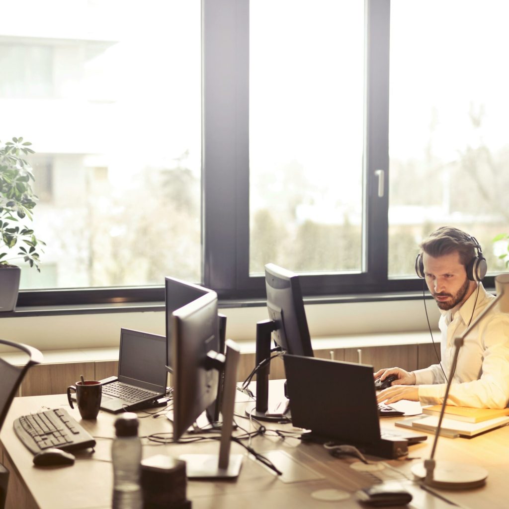 pexels-photo-845451-845451 A businessman sits at a desk using multiple computers and a headset in a well-lit modern office.